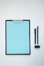 Clipboard With Blue Paper Near Pens
