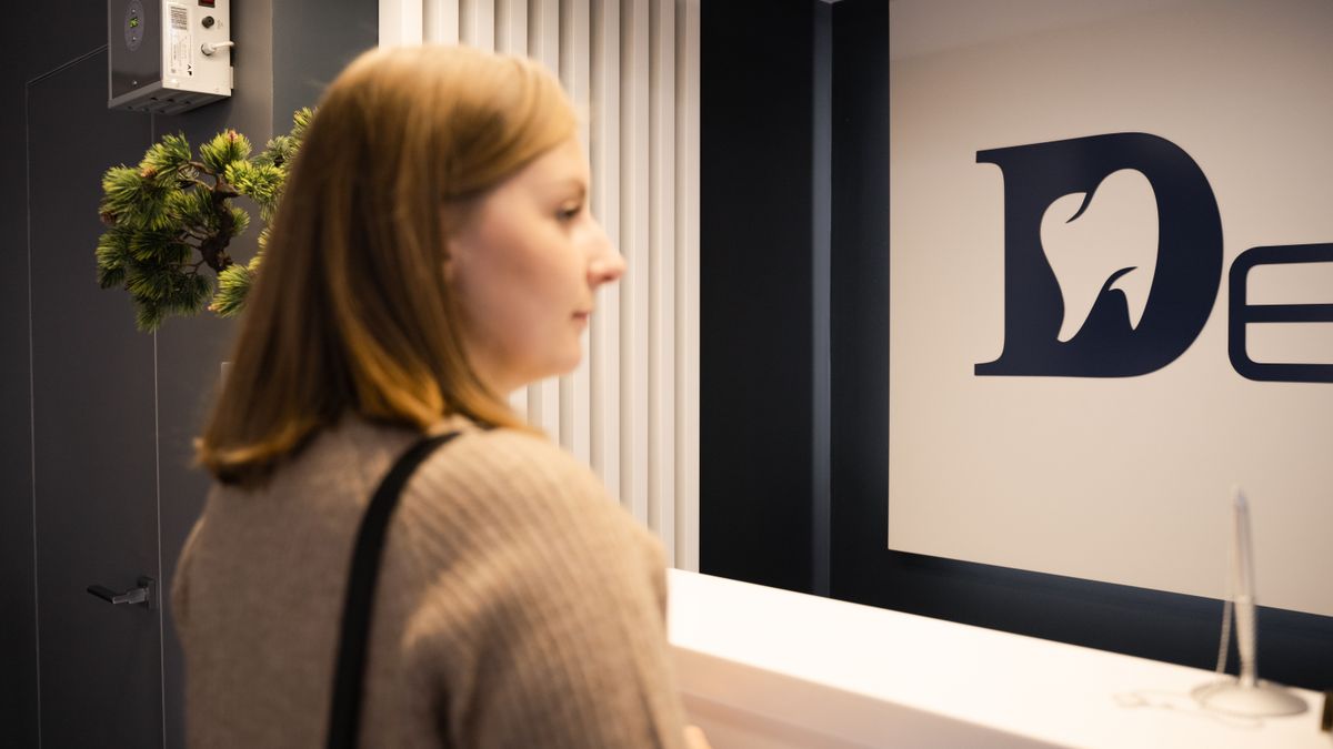 Young woman stands at a dental office reception, side view, casual attire.