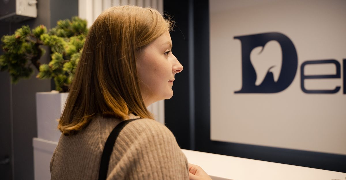 A woman waiting at the dental clinic reception, viewed from the side. Indoor setting.