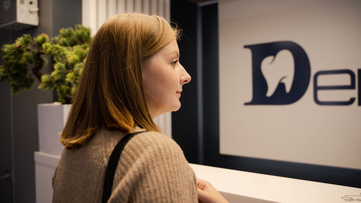 A woman waiting at the dental clinic reception, viewed from the side. Indoor setting.