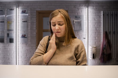 Woman in Brown Sweater With Hand Pressing on Her Cheeks