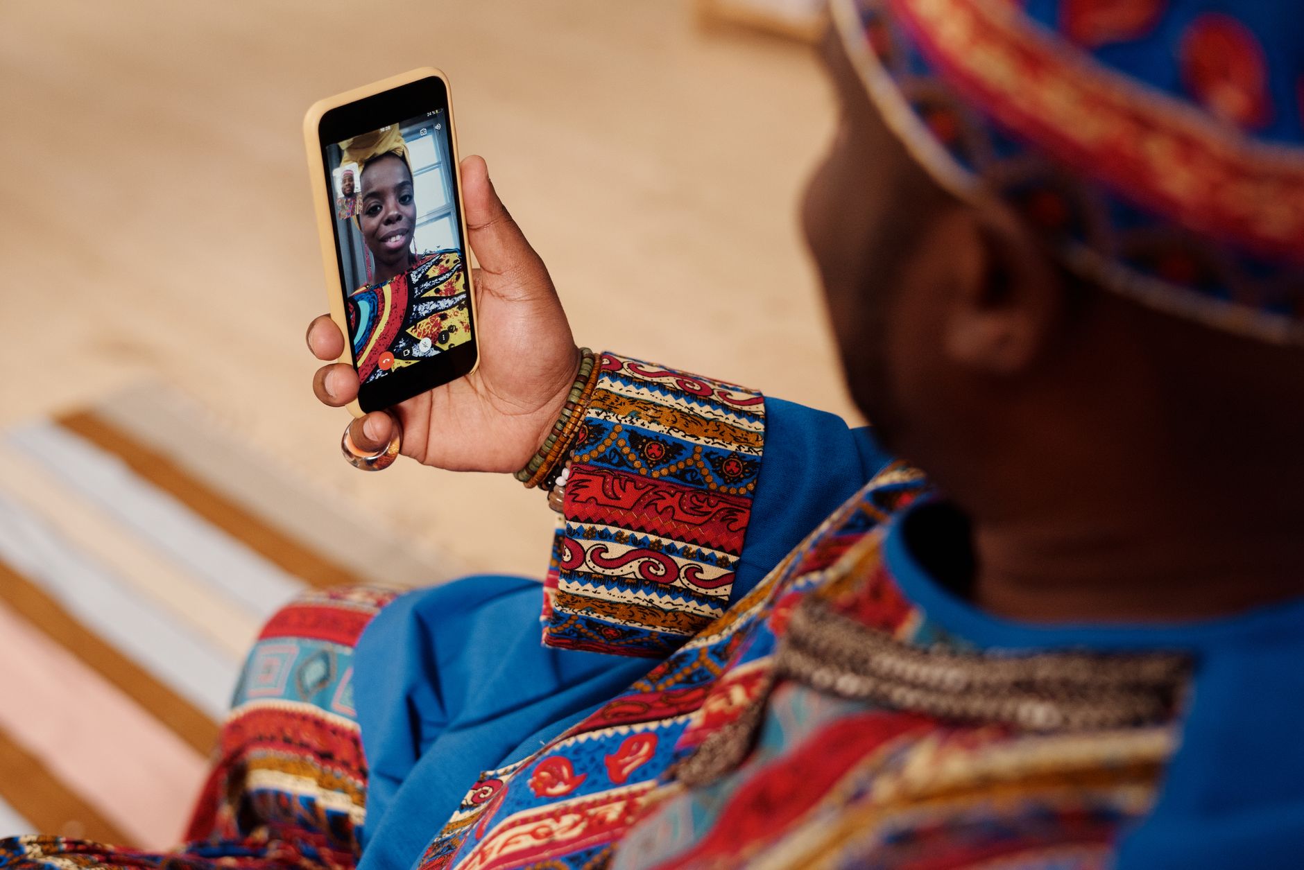 Hombre con vestimenta tradicional de colores sosteniendo un smartphone durante una videollamada con una mujer