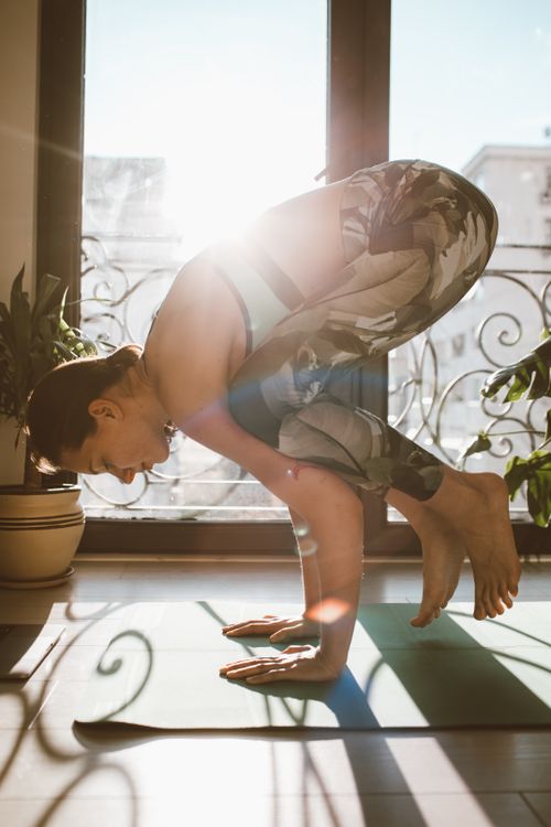 Free A woman performing a yoga pose indoors with sunlight streaming through a glass door. Stock Photo