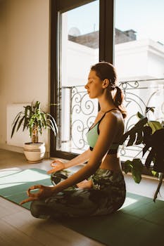 Woman meditating in lotus position on yoga mat indoors, capturing tranquility.