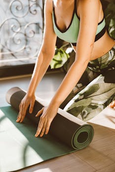 Woman rolling a yoga mat in a sunlit room, preparing for exercise.