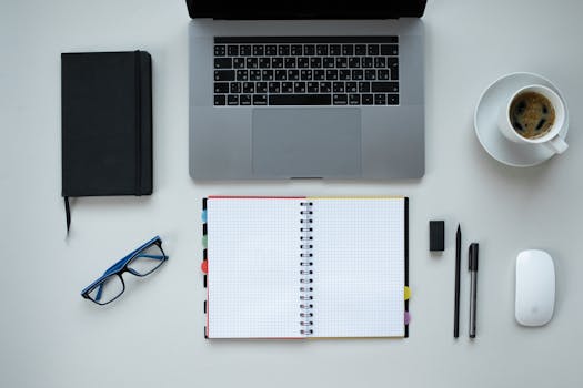 Top view of a desk with laptop, notebook, coffee, and office supplies, perfect for remote work theme.