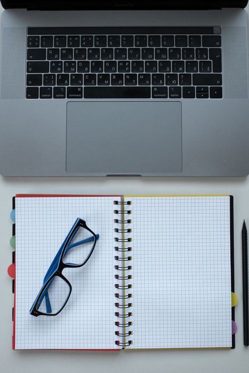Free Top view of a neat workspace featuring a laptop, notebook, and glasses for productivity. Stock Photo