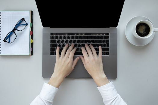 Top view of hands typing on a laptop with a cup of coffee and eyeglasses nearby on a desk.