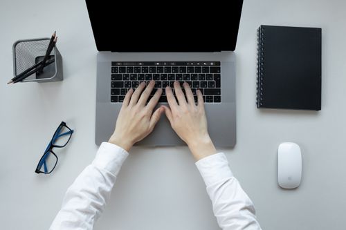 Free Person typing on a laptop at an office desk with accessories, emphasizing productivity. Stock Photo