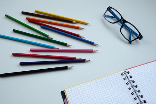 Colorful pencils arranged on a table with a notebook and glasses, ideal for education and creativity themes.
