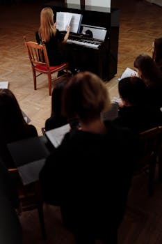 A choir practicing with a pianist in a dimly lit room, focusing on music sheets.