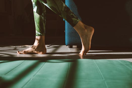 Bare feet stepping onto a yoga mat in a sunlit room with vibrant green leggings casting shadows.
