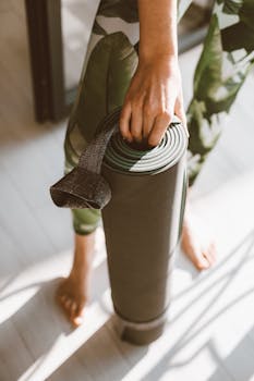 Person with rolled yoga mat and leggings, preparing for indoor exercise session.