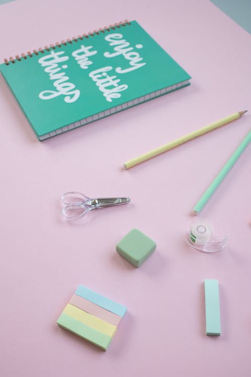 Green Spiral Notebook and Pencils on a Pink Surface