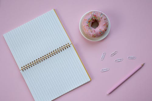 Doughnut on White Saucer Beside White Notebook