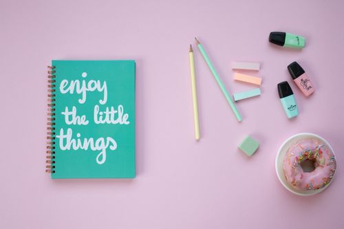 Free A vibrant flat lay of desk items with a positive message notebook and colorful donut on a pink background. Stock Photo