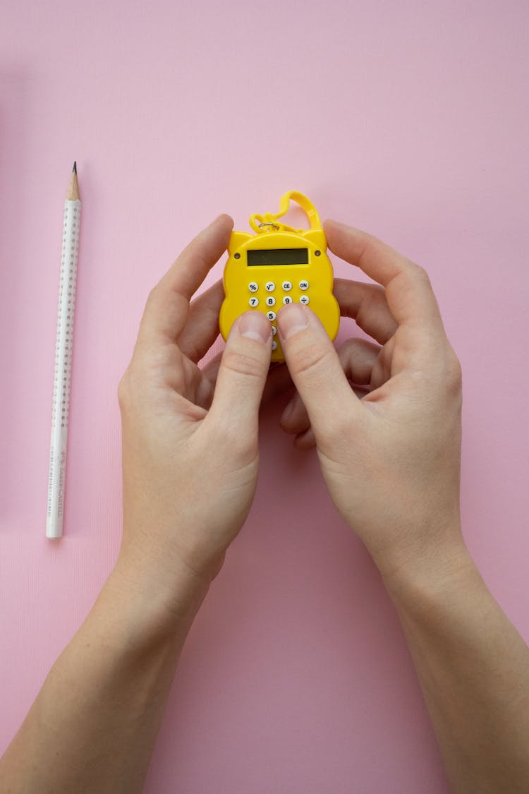 Hands Of A Person Holding A Yellow Miniature Calculator