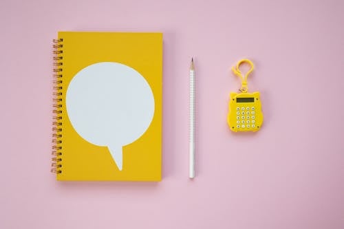 A Yellow Spiral Notebook and Calculator on a Pink Surface