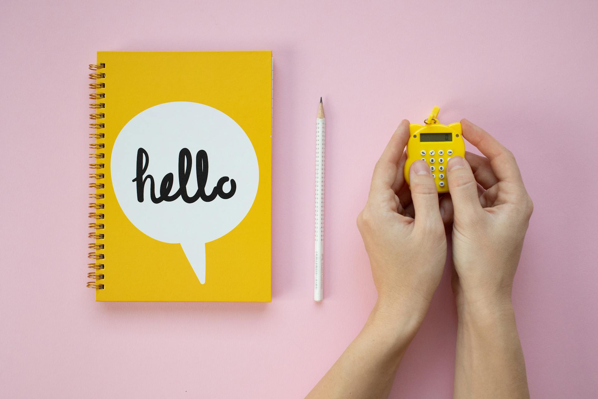 Yellow Notebook and Hand of a Person Holding a Yellow Calculator