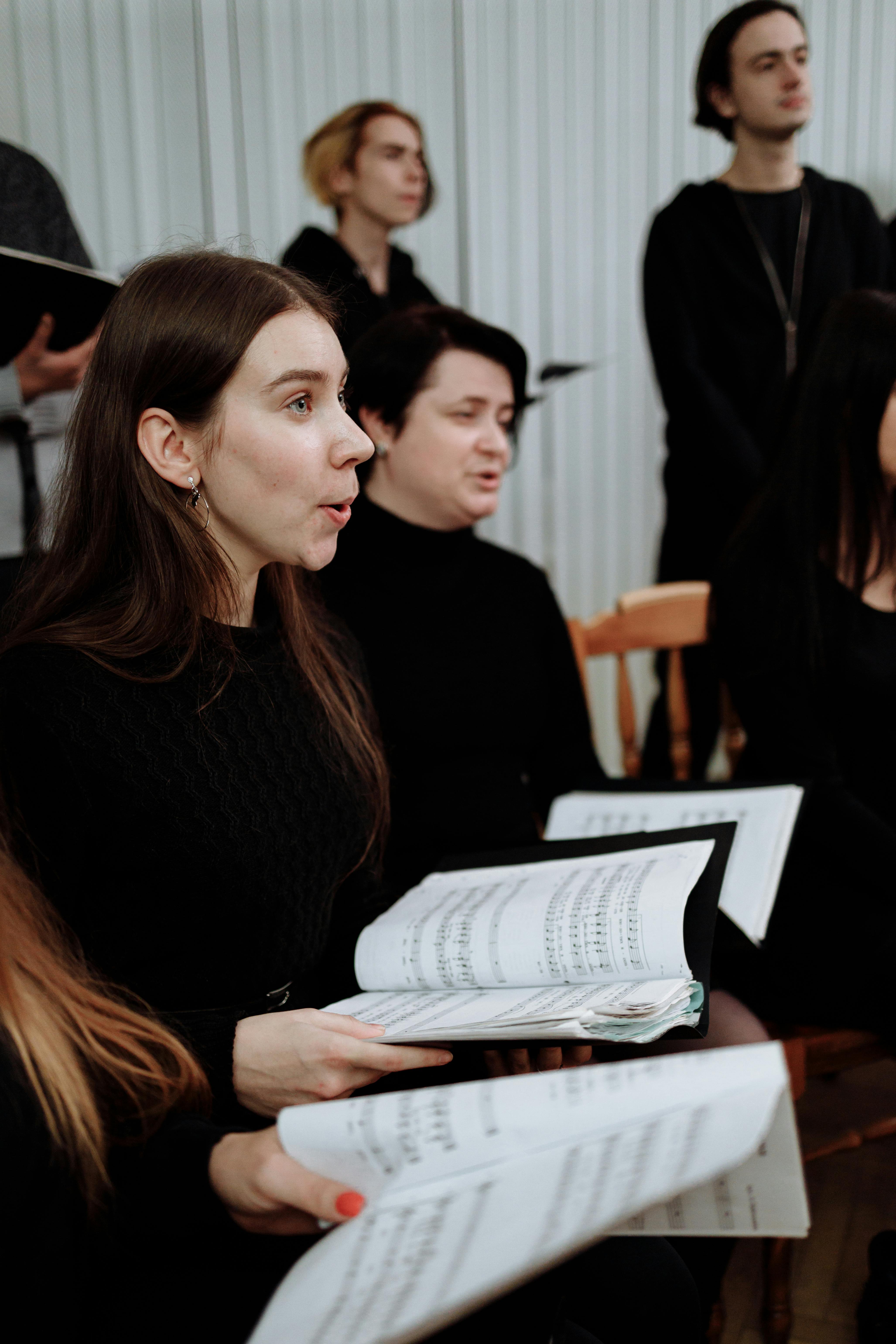 Free Women in a choir singing indoors, holding sheet music during a performance. Stock Photo