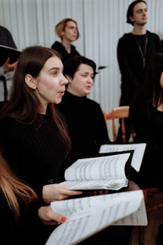 Women in a choir singing indoors, holding sheet music during a performance.