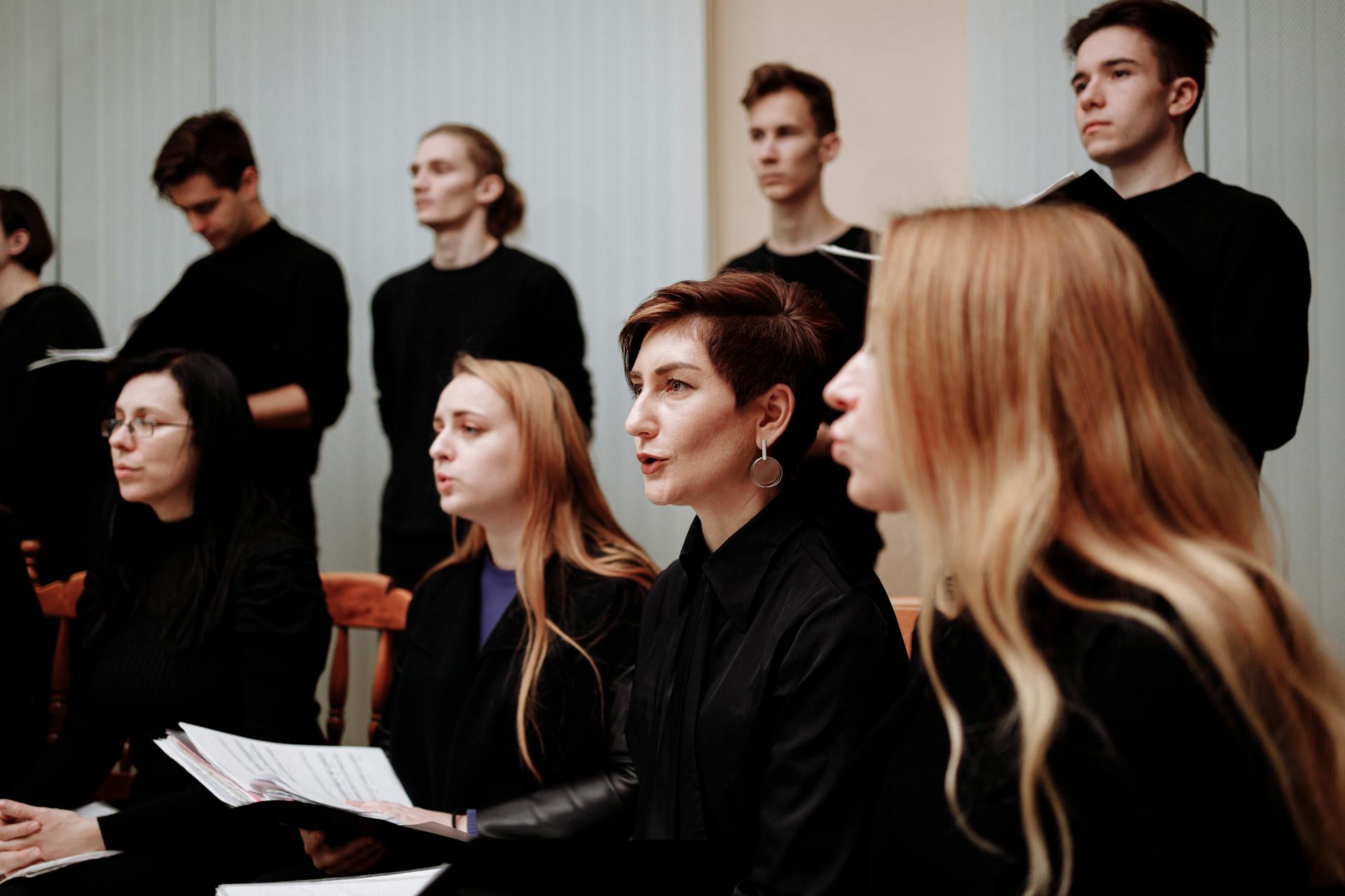 A group of diverse choir members singing passionately indoors, wearing black.