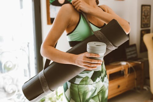 Woman Carrying a Rolled Yoga Mat and Holding a Cup