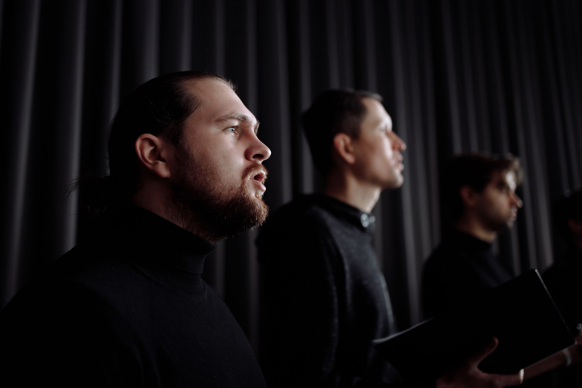 A group of male singers performing passionately indoors, dressed in dark attire, creating an elegant atmosphere.