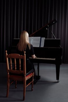 Blonde woman practicing piano indoors, captured in a dimly lit setting with focus on musical rehearsal.