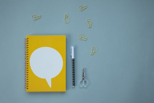 Free A Yellow Notebook and Bulb Shape Paper Clips Stock Photo