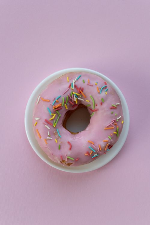 Free Delicious donut with pink icing and colorful sprinkles on a pastel pink background. Stock Photo