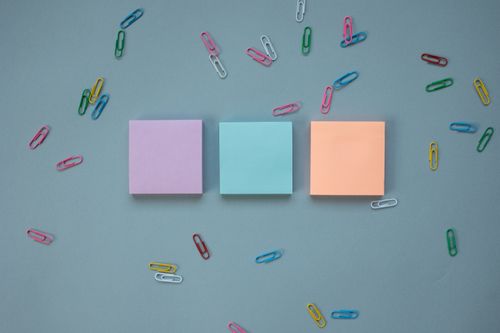 Free A flat lay of pastel sticky notes and colorful paper clips on a blue background. Stock Photo