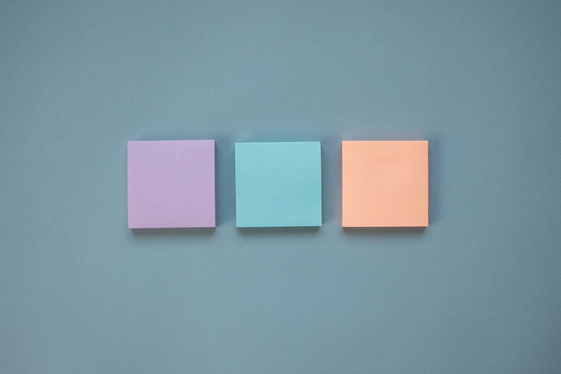 Three pastel-colored Post-It Notes arranged in a neat row on a blue backdrop.