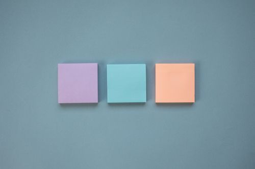Free Three pastel-colored Post-It Notes arranged in a neat row on a blue backdrop. Stock Photo