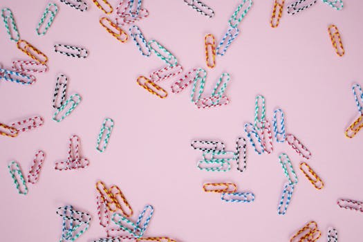 Vibrant paper clips scattered on a pastel pink background, creating a playful stationery scene.