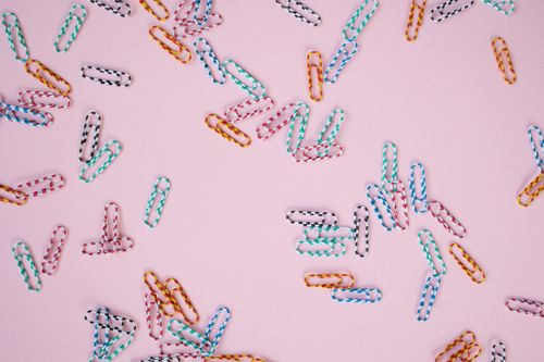 Free Vibrant paper clips scattered on a pastel pink background, creating a playful stationery scene. Stock Photo