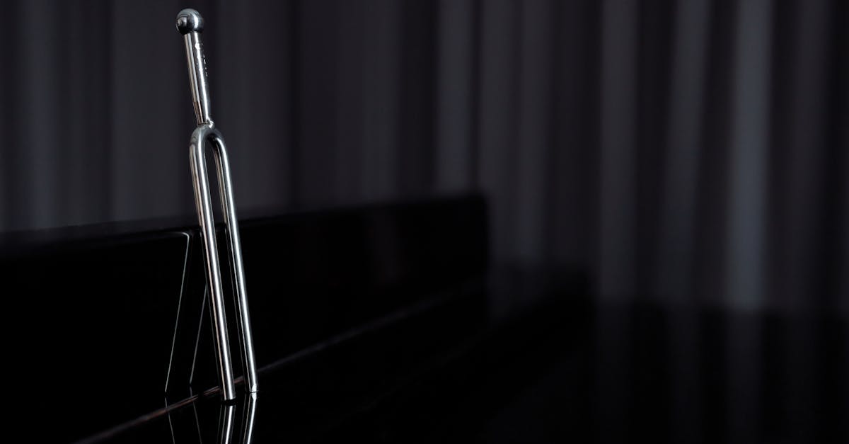 A close-up of a metal tuning fork standing on a reflective piano surface with dark background.