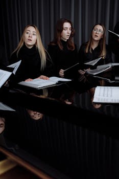 A group of women singing in a choir holding sheet music indoors, near a piano.