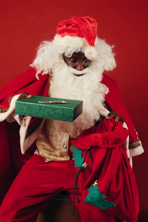 Free Black Santa Claus holding a green gift box, creating a warm Christmas vibe. Stock Photo