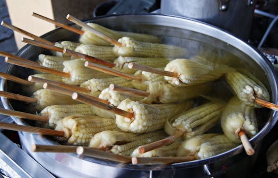 Freshly boiled corn cobs on sticks steaming in a large metal pot, capturing the essence of a healthy snack.