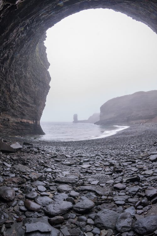 Wide angle of rocky cliff with wet boulders washed by foamy sea waves in overcast gloomy day