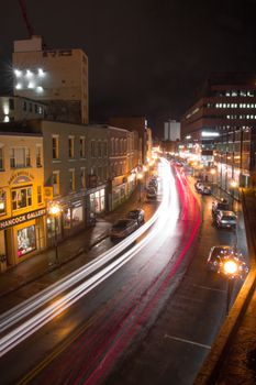 Glowing streetlamps on sidewalk of city with lights from moving cars in long exposure at night