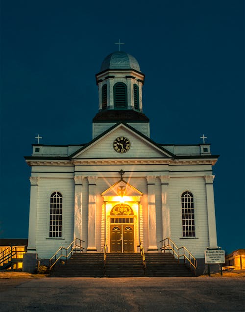 Facade of old Christian church with cross on top of dome with glowing light under door at night