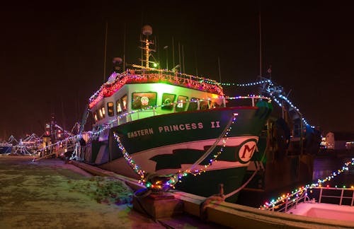 Ship with mast decorated with colorful glowing Christmas garlands moored on quay at dark night