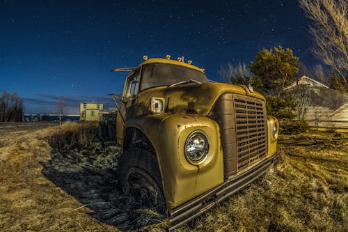 Wide angle of damaged old fashioned truck on grassy lawn in countryside under starry sky at dusk