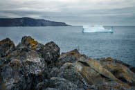 Glacier in rippled sea against mountains under cloudy sky