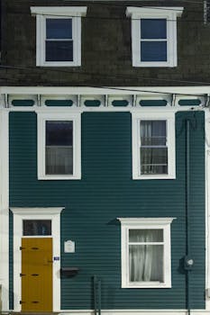 Modern house exterior featuring teal walls and a striking yellow door in an urban setting.
