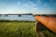 Old cannon on grass shore against sea and mountains