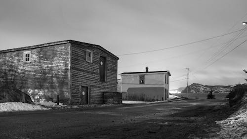 Black and white of aged building exteriors against roadway and mounts under cloudy sky in winter