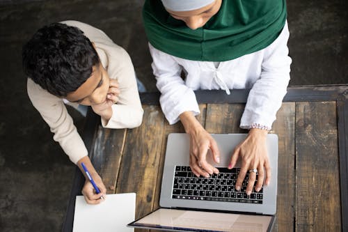 Arabian mother in hijab typing report on laptop near son